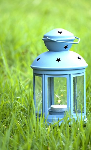 Linterna azul, con vela encendida en el interior, sobre hierba verde
  - Foto, imagen
