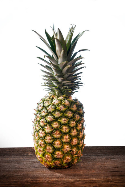 Big tropical pineapple with its leaves on a barn wood board on white background - Foto, immagini