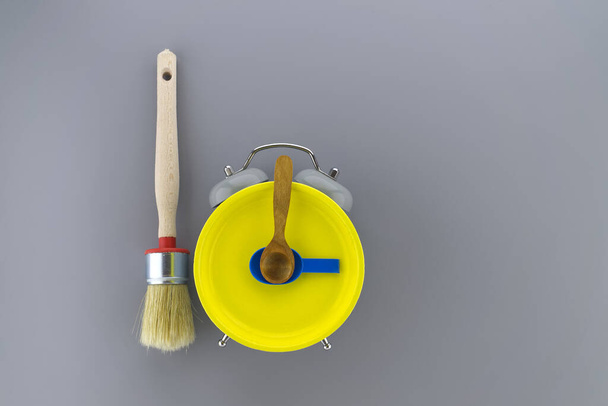 Creative DIY, decorating or renovations background with two clean bristle brushes and a colorful yellow alarm clock with tools for hands forming a border on grey with copy space - Fotografie, Obrázek