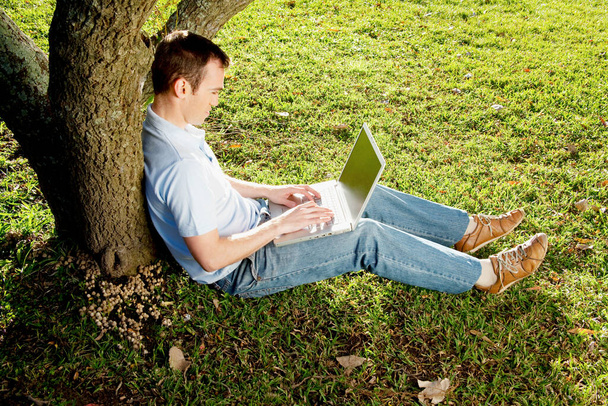young man sitting on grass and working on laptop - Valokuva, kuva