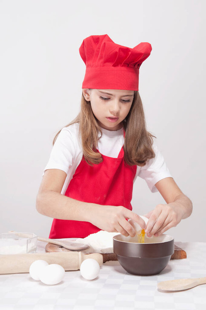 little girl in a white apron and a hat with a red cap and a blue sweater on a light - 写真・画像