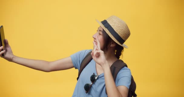 Feliz juventud hermosa mujer de Asia viajero usar sombrero de gafas de sol y mochila sonriente uso smartphone mirar a la cámara tomar selfie en el espacio vacío fondo amarillo. Concepto de felicidad positiva. - Metraje, vídeo