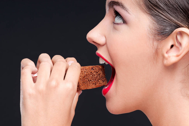 young woman eating chocolate chips on black background - Foto, imagen