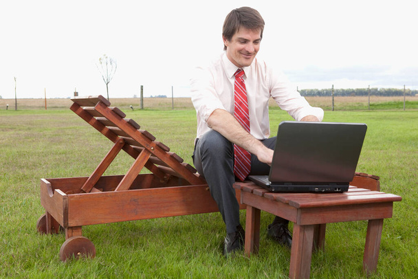 businessman sitting on a bench and working on a laptop - Fotó, kép