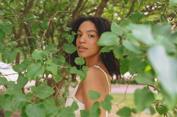 Móda zblízka portrét smyslné atraktivní mladé přirozeně krásné Afroameričanky s afro vlasy pózující v přírodním parku v zeleném listoví. - Fotografie, Obrázek