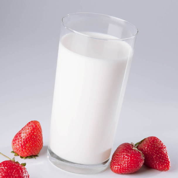 glass of milk and fresh strawberries on white background - Foto, afbeelding