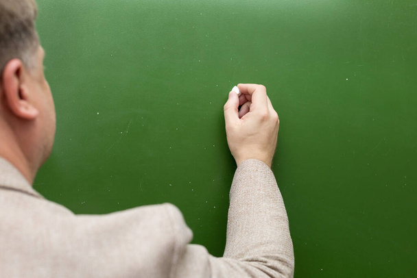 A man's hand with chalk on a green blackboard background copy the space. - Photo, Image
