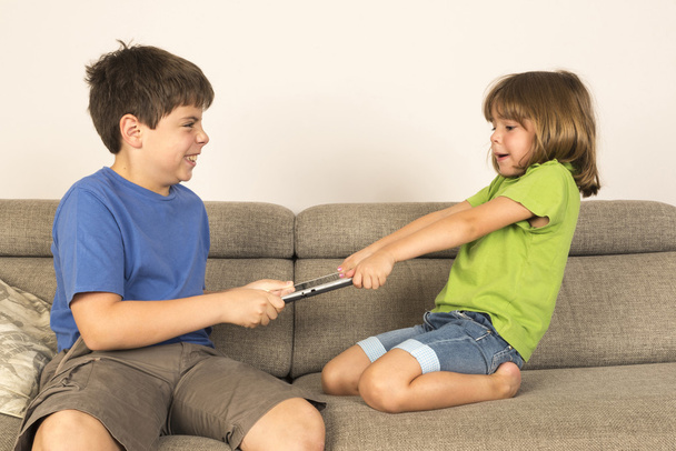 Kinder streiten für das Spielen mit einem digitalen Tablet auf dem Sofa. - Foto, Bild