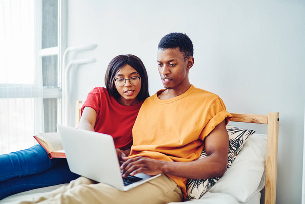 Millennial marriage enjoying internet communication via laptop computer during weekend in home apartment, African American wife and husband choosing web movie for online watching on leisure - Fotó, kép