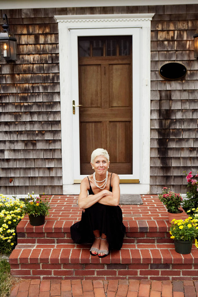 Portrait of a senior woman sitting at the front stoop of house - Fotó, kép