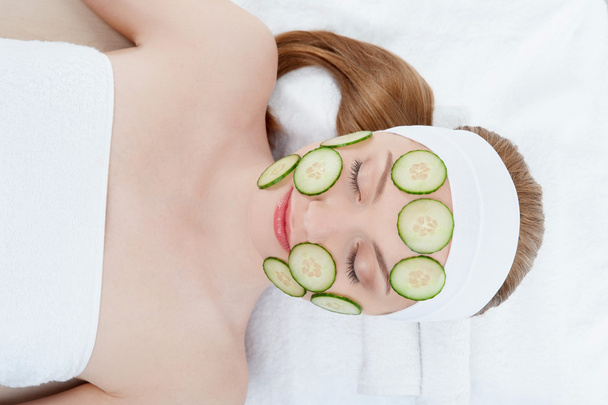 Beautiful young woman receiving facial mask of cucumber in beaut - Valokuva, kuva