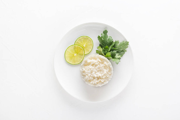 Gekochter Reis mit Zitronen- und Petersilienblättern in einem weißen Teller auf hellem Hintergrund. Blick von oben - Foto, Bild