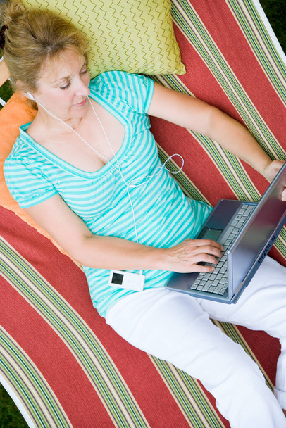 High angle view of a mature woman using a laptop while listening to music in a hammock - Foto, Bild