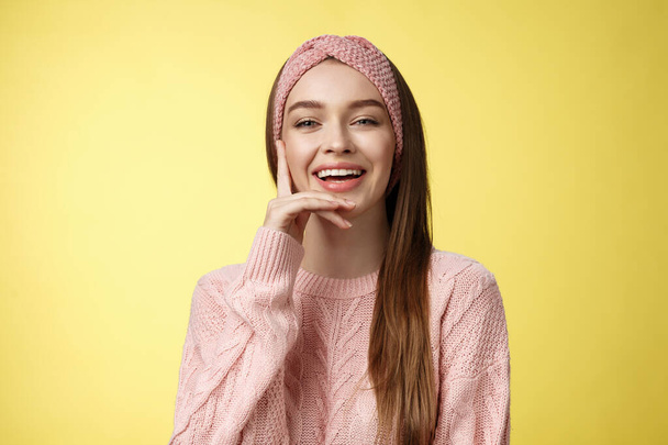 Cheerful entertained young attractive european woman in knitted pink headband, sweater touching cheek smiling, laughing. Student with smile on face, having fun, giggling over comedy movie - Фото, изображение