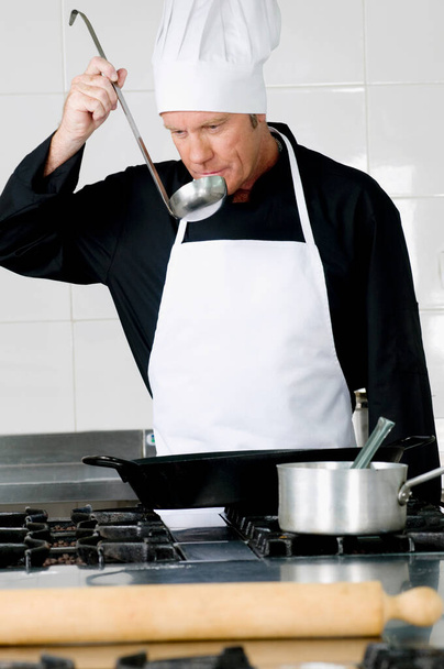chef in a kitchen with a knife and a pan - Foto, afbeelding
