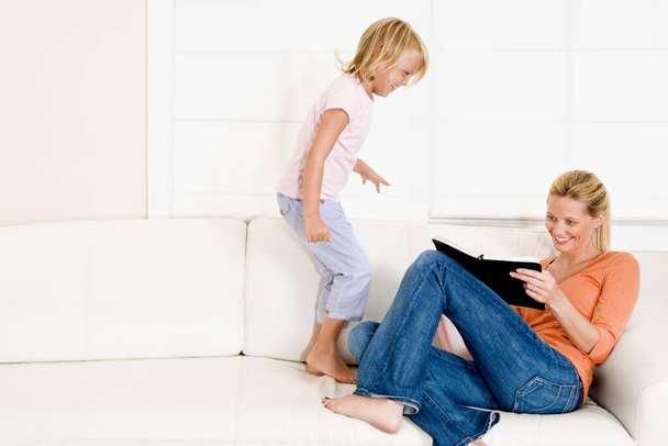 mother and daughter sitting on sofa and looking at tablet - Foto, afbeelding