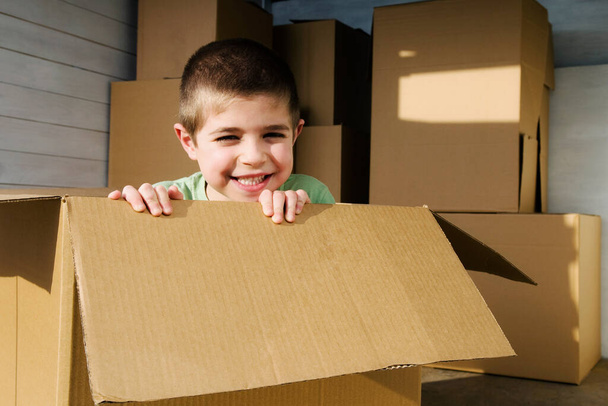happy boy with cardboard boxes and looking at camera - Φωτογραφία, εικόνα