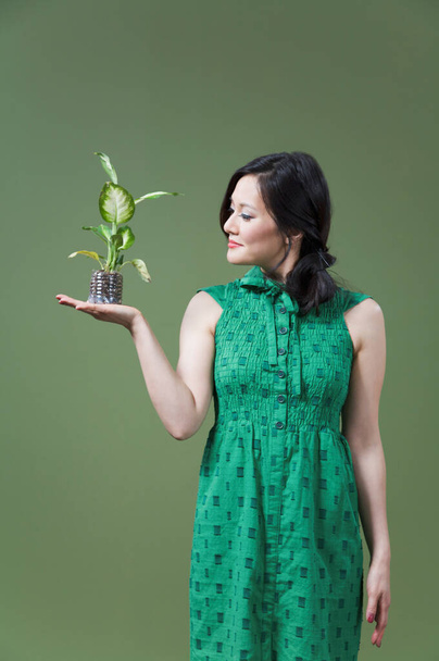 young beautiful woman in green dress holding a plant in her hands - Foto, imagen