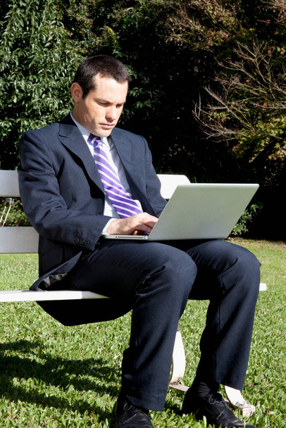 businessman sitting on a bench and working on a laptop - Zdjęcie, obraz