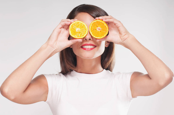 young beautiful woman with orange eyes and yellow lips holding a slice of lemon on her face, isolated on - Photo, image