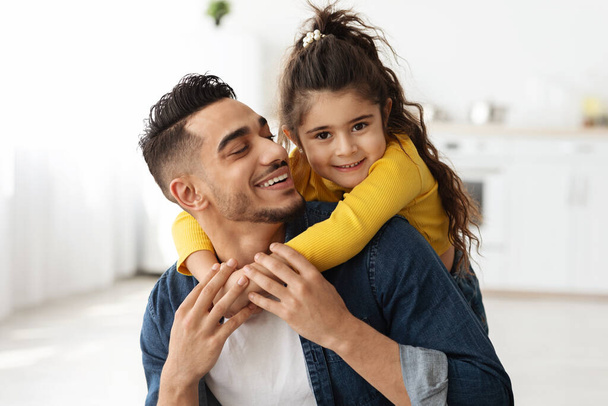 Крупный план счастливого отца со стороны Среднего Востока и маленькой дочери, обнимающейся дома - Фото, изображение