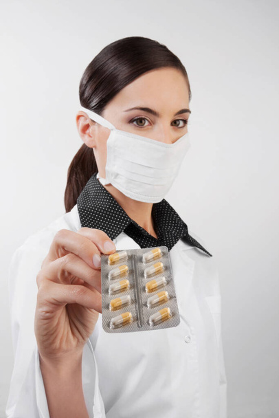 young woman in medical mask and gloves holding a pill isolated on white background - Foto, afbeelding