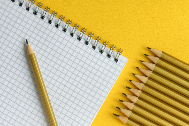Simple pencils and a notebook in a cage close up, yellow background, top view - Zdjęcie, obraz