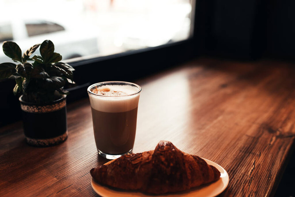 Cup of coffee, croissant at table near the window in cafe. Blurred background. High quality photo - Zdjęcie, obraz