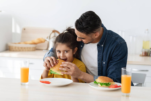 A los papás les importa. joven árabe padre alimentación poco hija con sándwich en cocina - Foto, Imagen