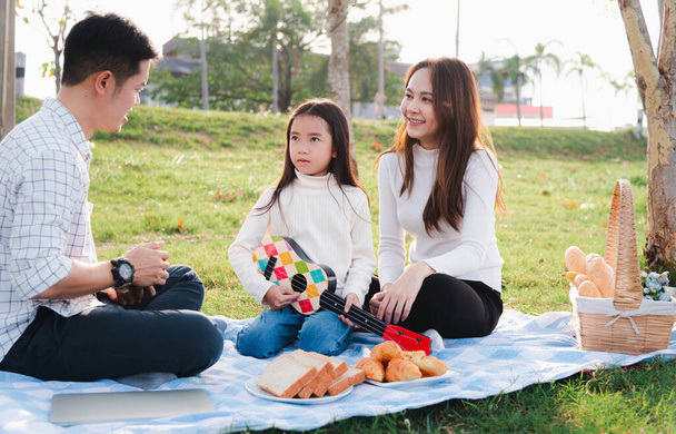 Happy Asian young family father, mother and children having fun and enjoying outdoor together sitting on the grass party with playing Ukulele during a picnic in the garden park on a sunny day - Фото, зображення