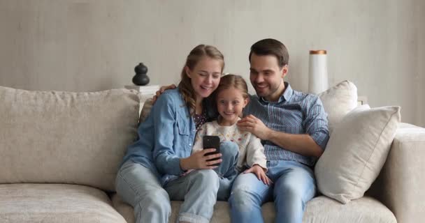 Couple and daughter having fun using mobile application on cellphone - Filmati, video
