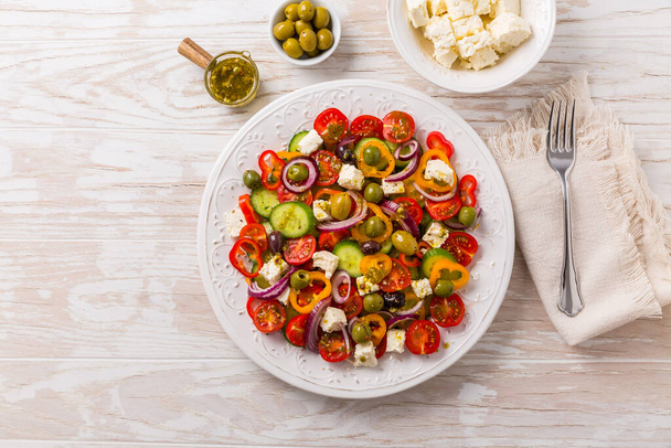 Greek salad of fresh cucumber, tomato, sweet pepper, lettuce, red onion, feta cheese and olives with olive oil dressing. Healthy food, top view - Foto, immagini
