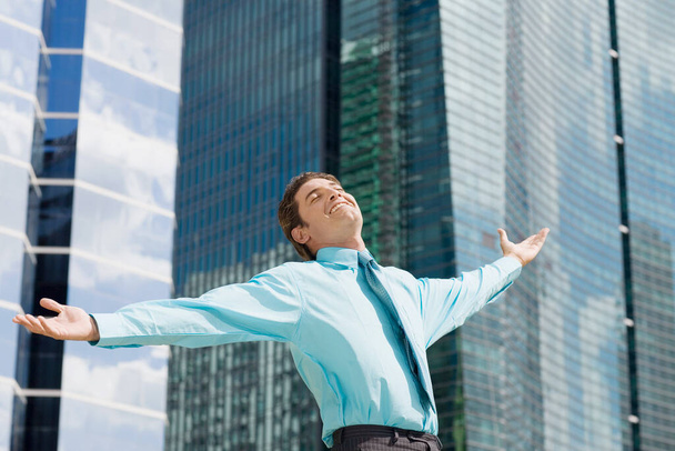 young businessman with arms crossed against blue sky - Foto, Bild