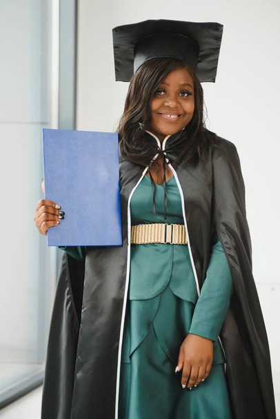 Happy Indian university student in graduation gown and cap holding diploma certificate. Portrait of mixed race Asian Indian and African. - Foto, imagen