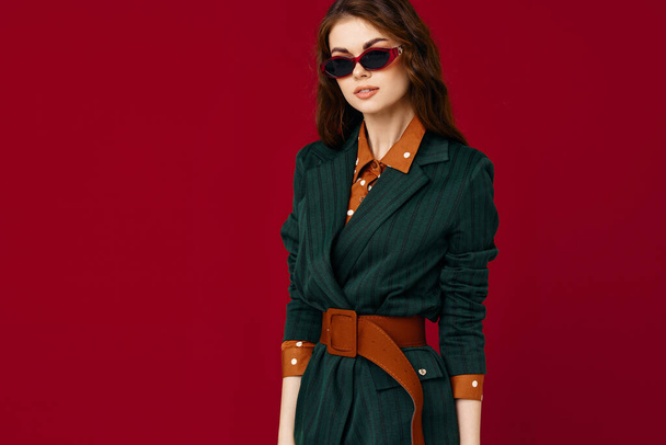 Güneş gözlüklü kadın ceketli moda stüdyosu kırmızı arka plan - Fotoğraf, Görsel