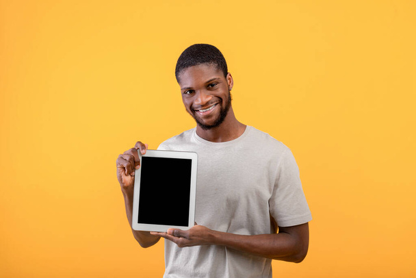 Young black guy showing digital tablet with blank screen, recommending website or mobile application, yellow background, - Фото, зображення