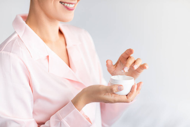 Sluiten van glimlachende vrouw met crème pot buis - Foto, afbeelding
