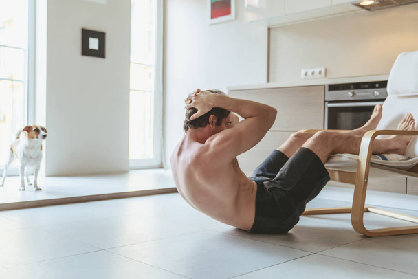Молодой человек во время занятий спортом дома в квартире на заднем плане кухни. - Фото, изображение