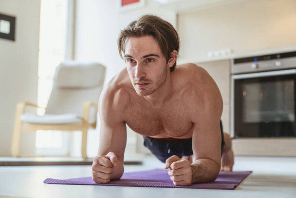 Young man during sports at home in the apartment on the background of the kitchen. - Fotoğraf, Görsel
