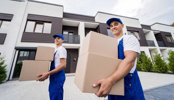 Two removal company workers unloading boxes into new customers home - Фото, изображение