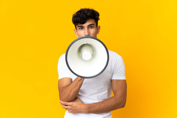 Giovane uomo argentino isolato su sfondo giallo urlando attraverso un megafono per annunciare qualcosa - Foto, immagini