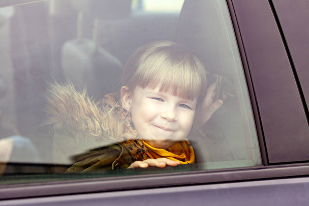 Kislány, gyerek ül a kocsiban kívülről nézve. Fiatal srác kukucskál a kocsi ablakán, portré, közelkép. Közlekedési eszközök, utazó gyermekek, szállítás, utazási betegség - Fotó, kép