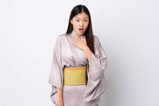 Молодая китаянка в кимоно на изолированном фоне удивлена и шокирована, глядя направо - Фото, изображение