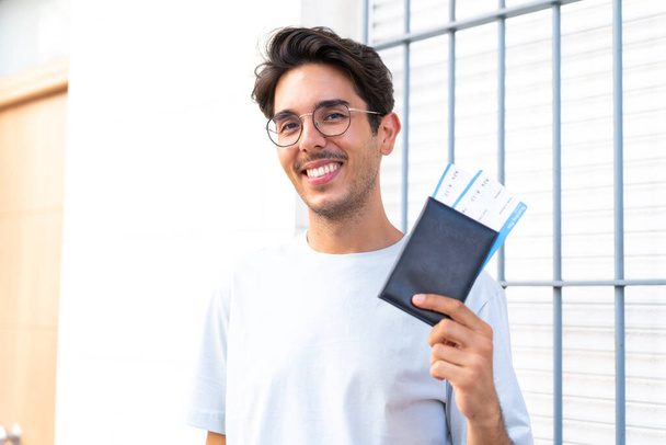 Jovem caucasiano ao ar livre feliz em férias com passaporte e bilhetes de avião - Foto, Imagem