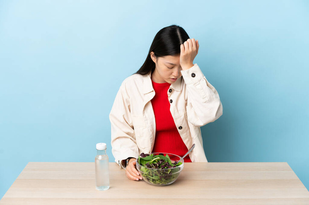Jeune fille chinoise manger une salade avec mal de tête - Photo, image