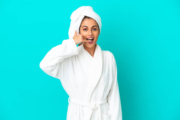 Young woman in a bathrobe over isolated blue background making phone gesture. Call me back sign - Foto, Imagem