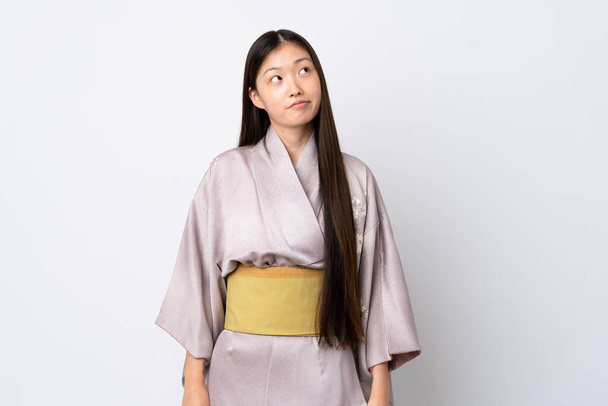 Mladý číňan dívka na sobě kimono přes izolované pozadí a vzhlíží - Fotografie, Obrázek