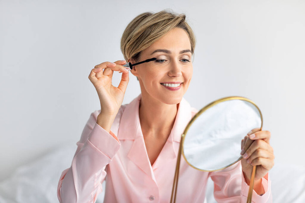 Gros plan de femme souriante tenant mascara appliquant le maquillage - Photo, image