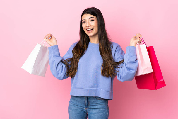 Junge Brünette Mädchen über isoliertem rosa Hintergrund mit Einkaufstaschen und Lächeln - Foto, Bild