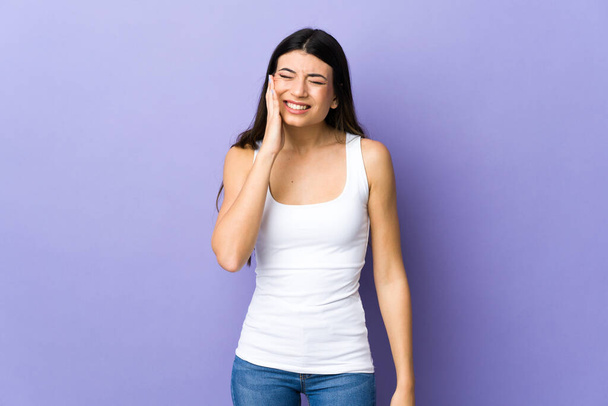 jonge brunette vrouw over geïsoleerde paarse achtergrond met kiespijn - Foto, afbeelding